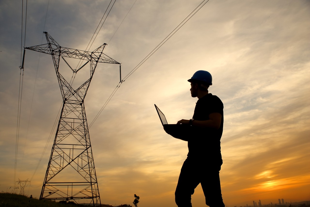 silhouette of electrical engineer on laptop computer inspecting transmission tower at sunset