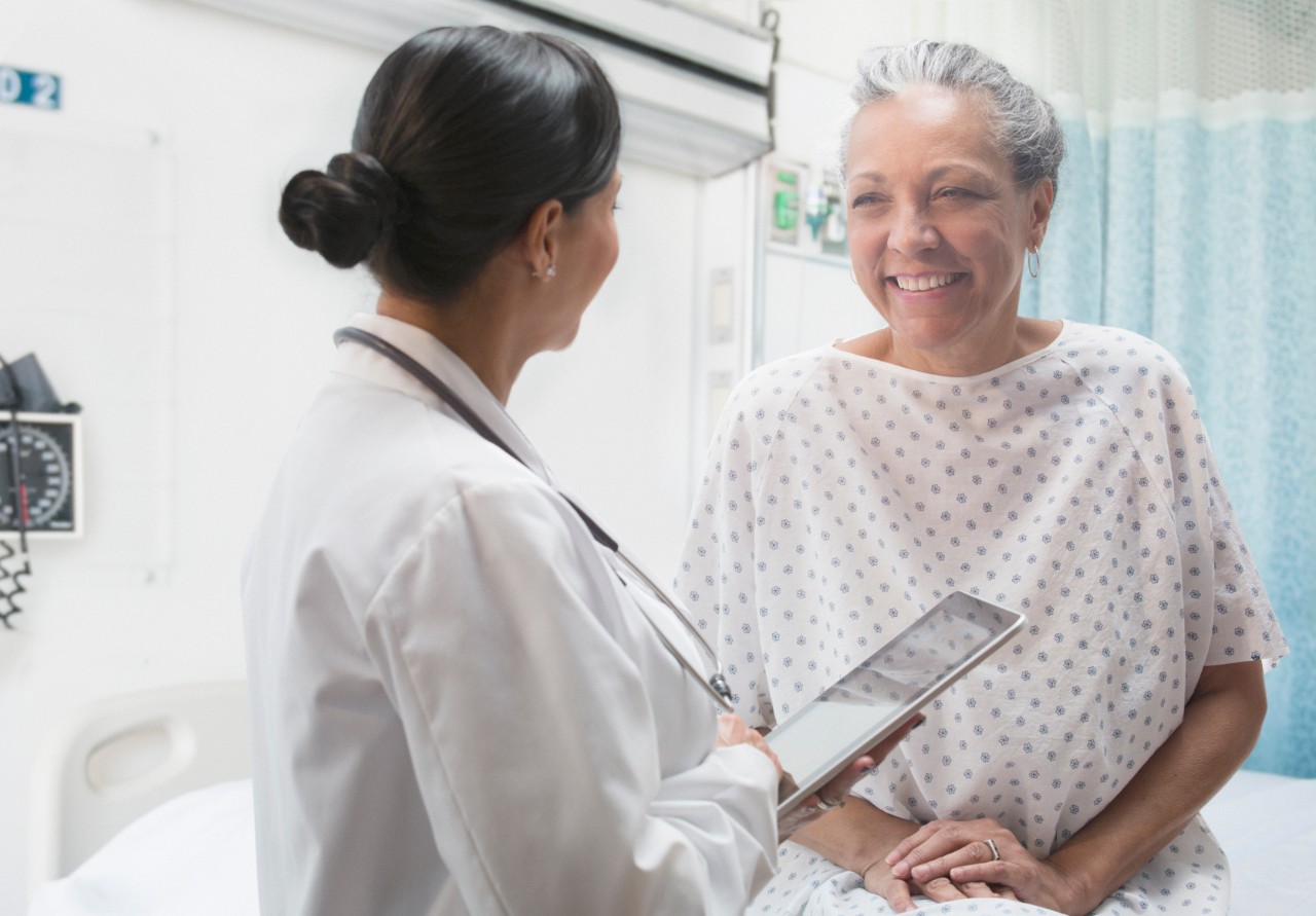 Hispanic doctor using digital tablet and talking to older patient